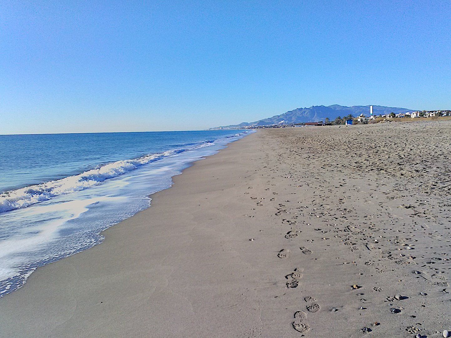 on the shoreline looking south along the sandy beach with footprints in the sand