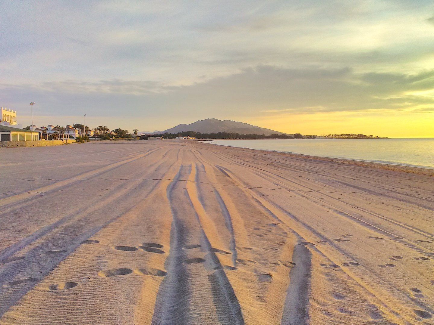 a wide expanse of sandy beach at sunrise and the white sand is tinged with orange from the sunrise