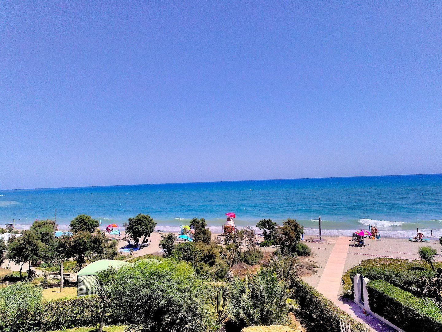 looking down onto beach from the terrace on a hot summer day blue sea blue skies and people on the beach sunbathing in the distance