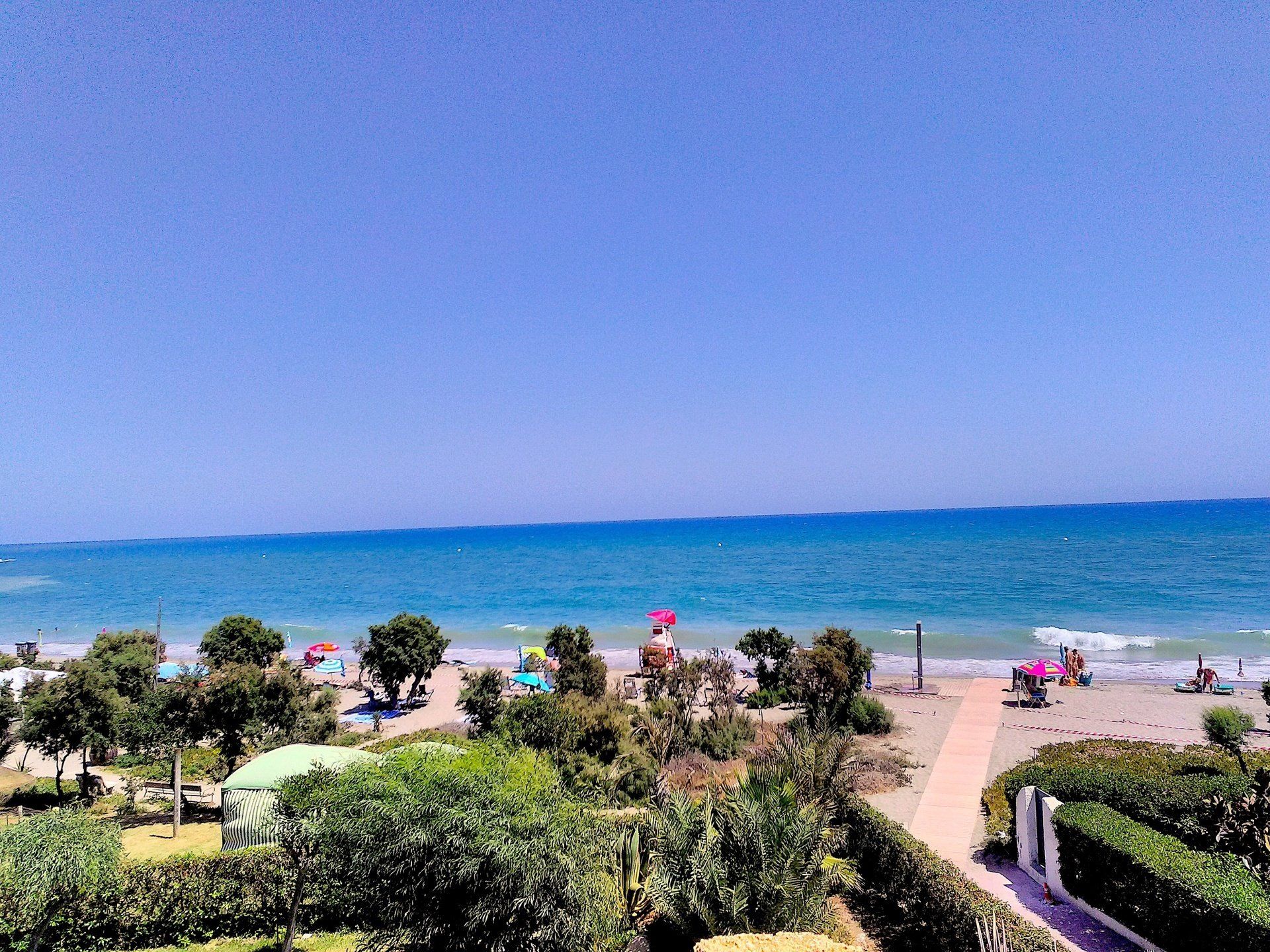 looking from the terrace and across the beach below and out to sea on a hot day with clear blue skies and blue sea