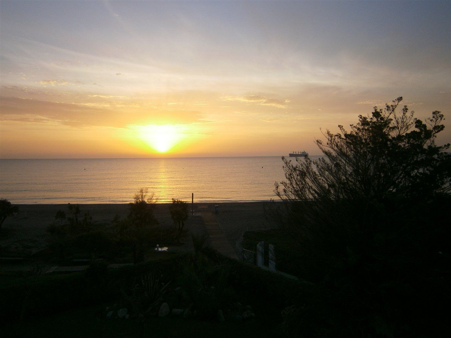 a beautiful yellow and orange cone shaped sun is rising from the sea with the orange refelcting on the water