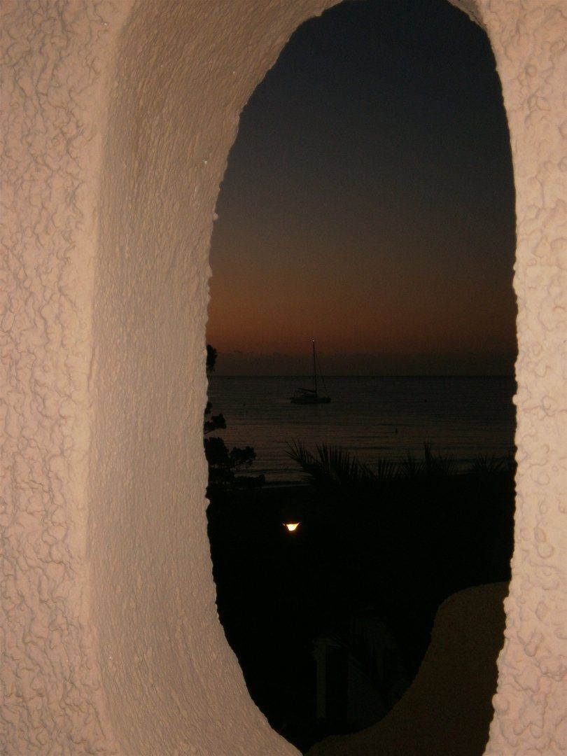 at dawn looking through the porthole in the wall where you can see a sailing boat at sea