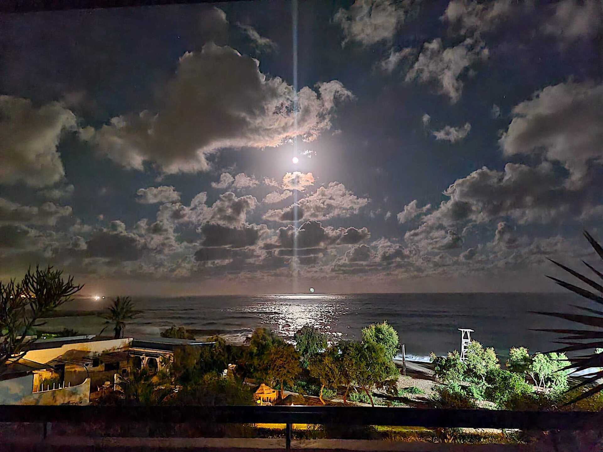 looking out across the beach and out to sea at night with the full moon lighting the water up