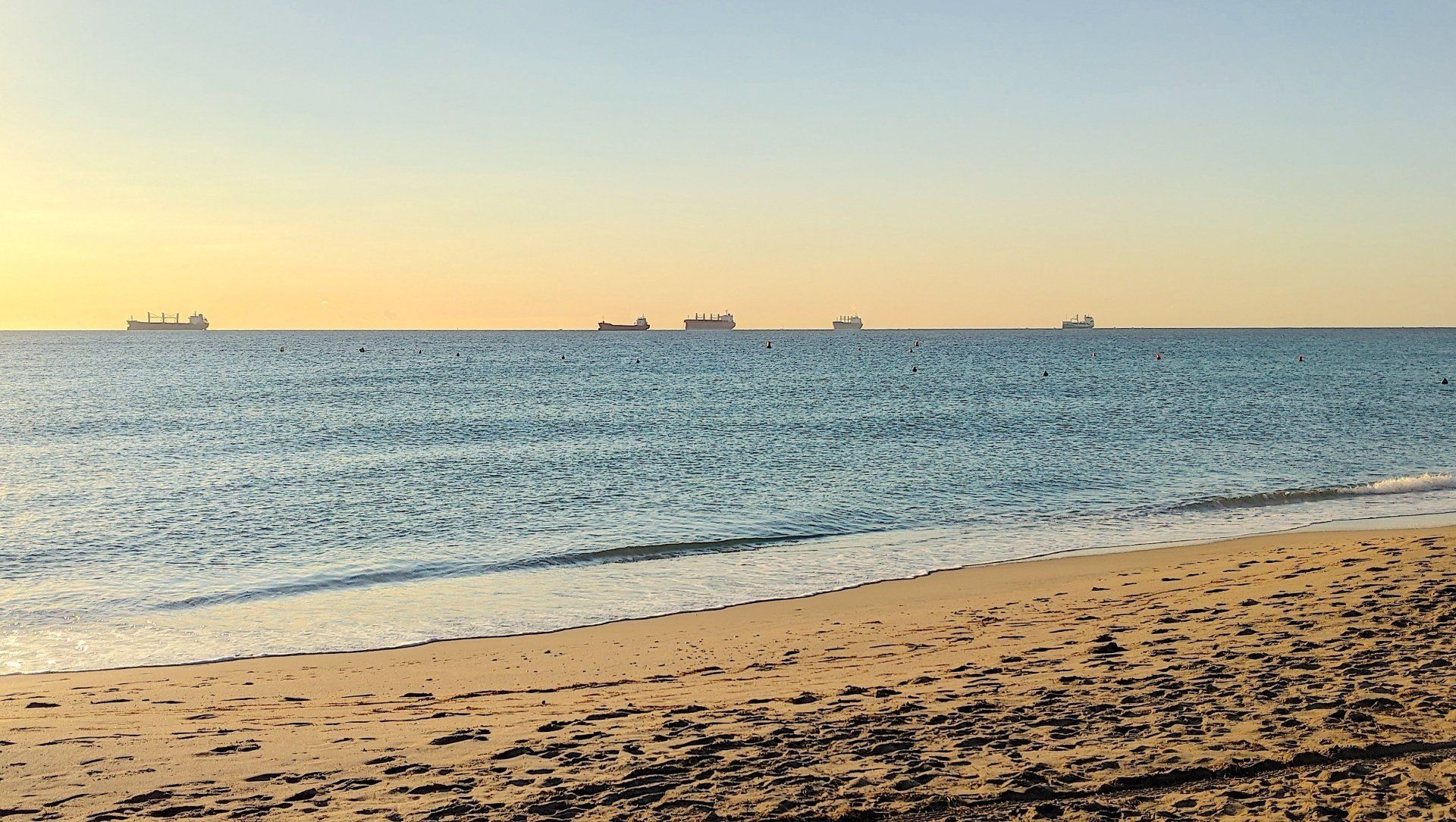looking from the sand out to sea there are four ships in a line on the horizon