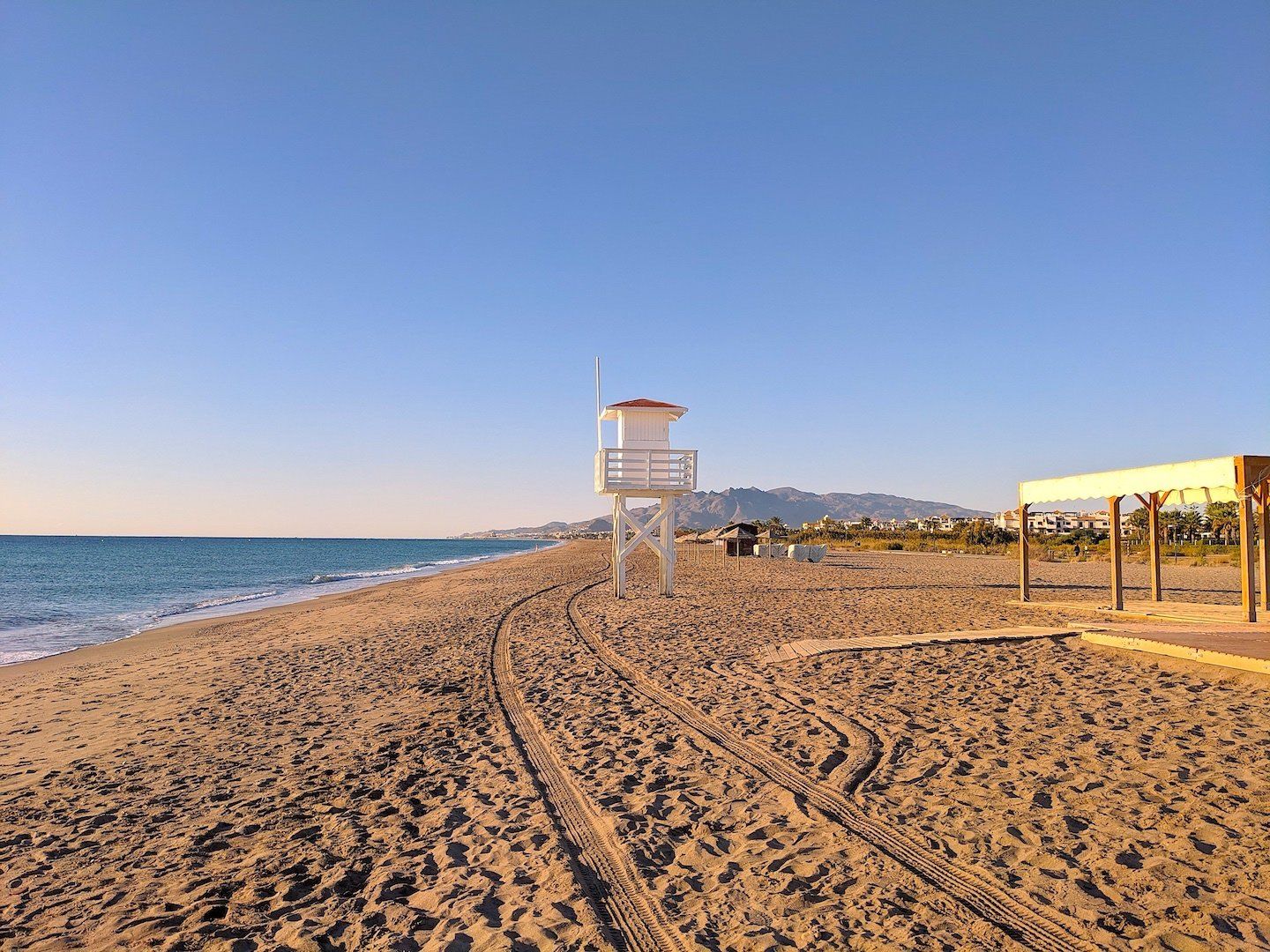 sandy beach stretching away with tyre tracks and a white tall wooden lifeguard tower in the centre