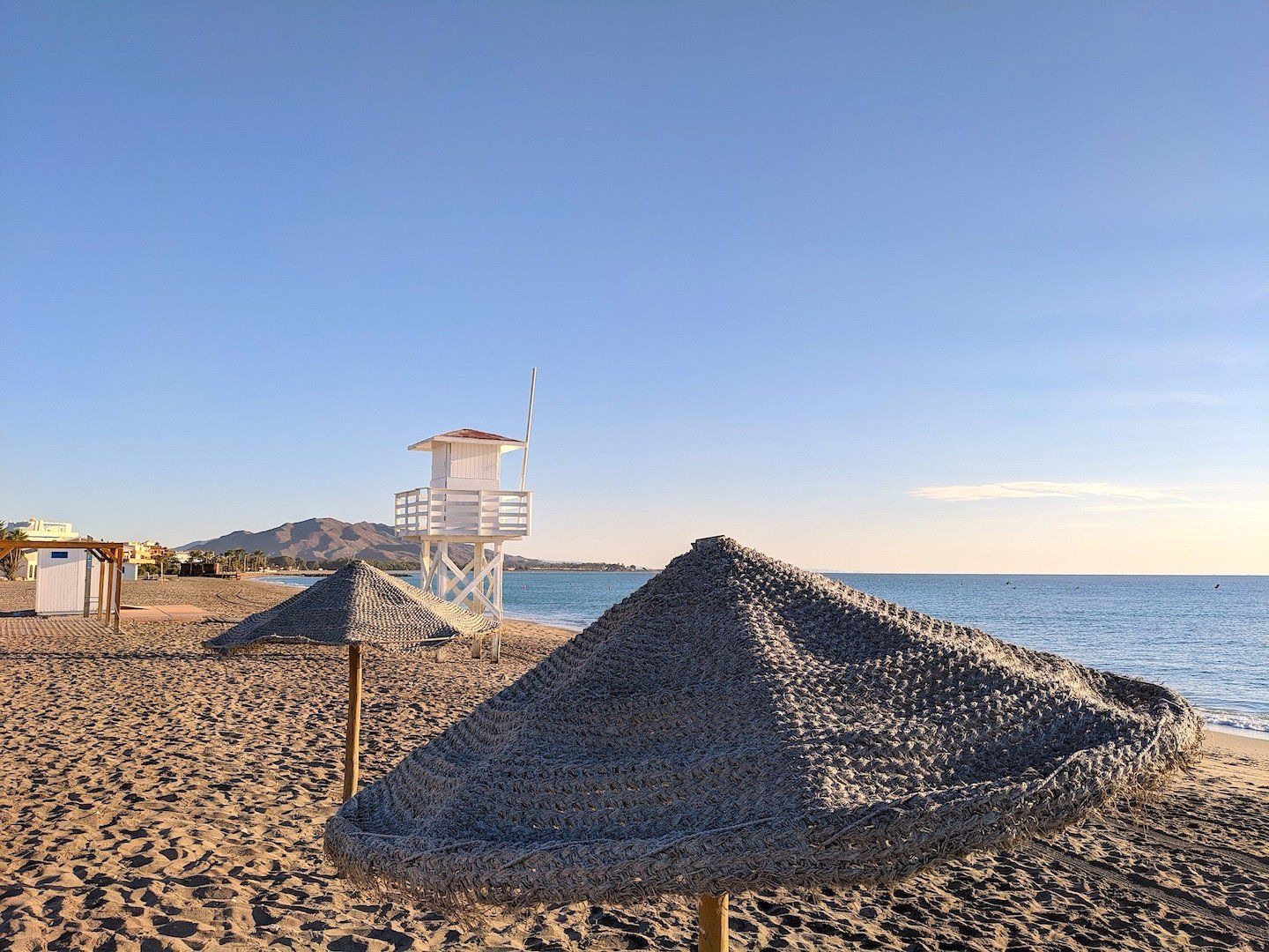 on the beach looking over the top of a thatched sun umbrella and a line of thatched umbrellas and the lifeguard tower beyond
