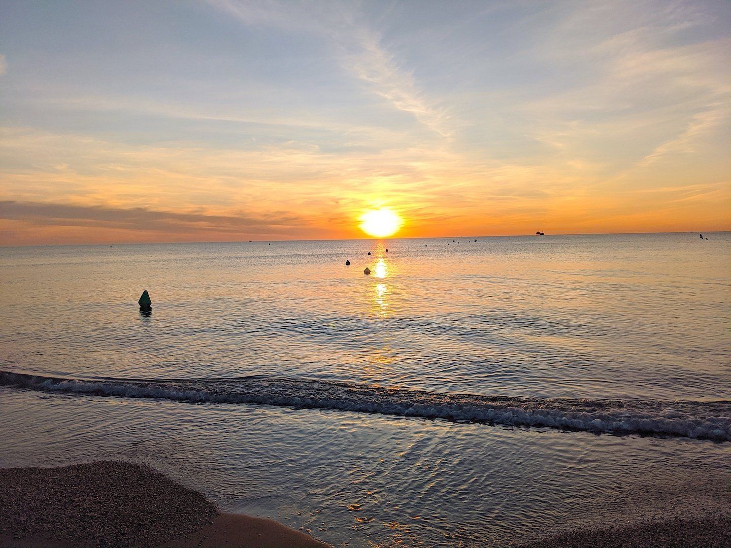 from the shoreline looking across the water at dawn while the sun rises on the horizon and the buoys float on the water