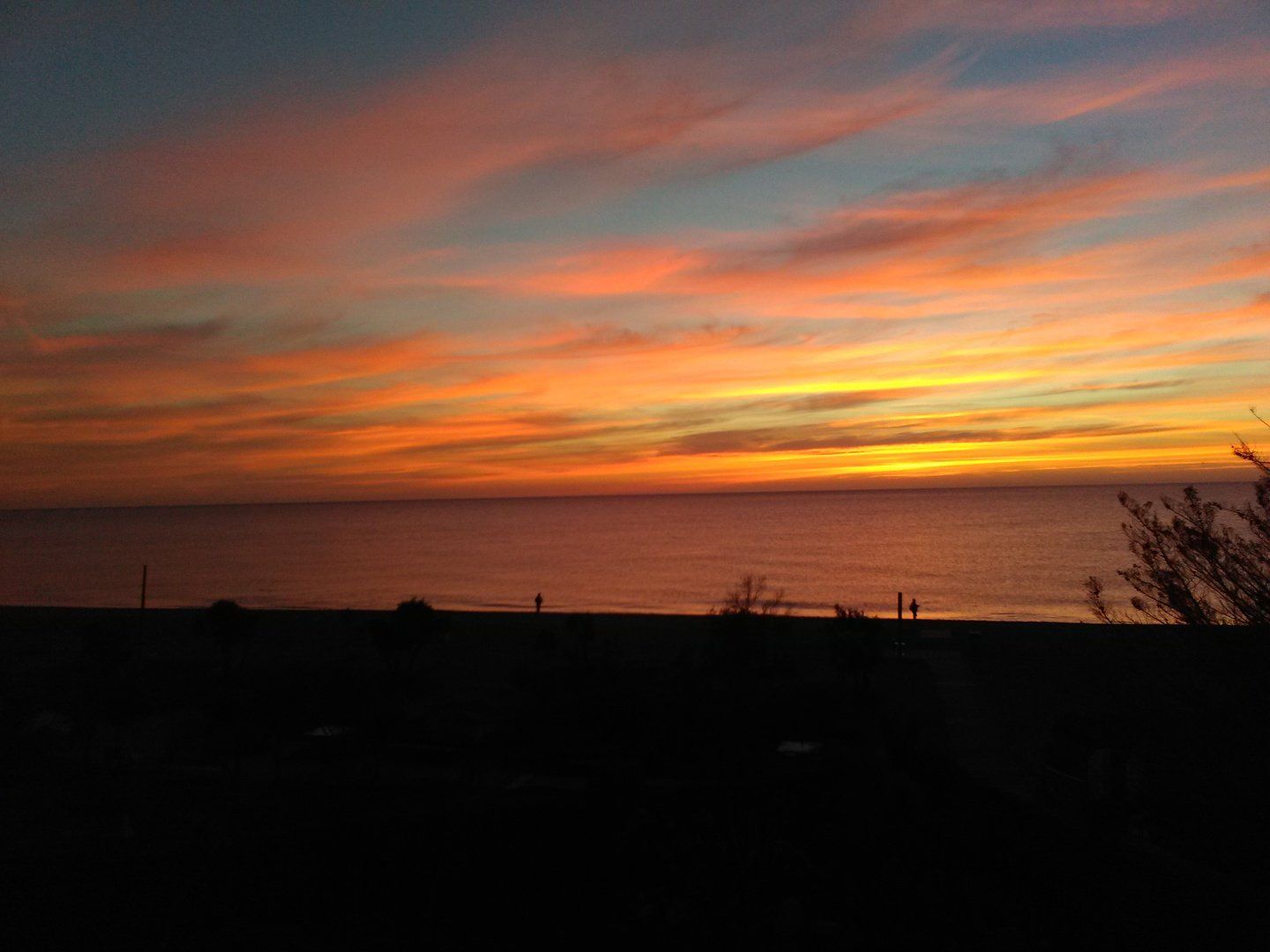 at dawn the sun is not yet in view but it lights up the sky in orange and you can just see some fishermen on the shoreline
