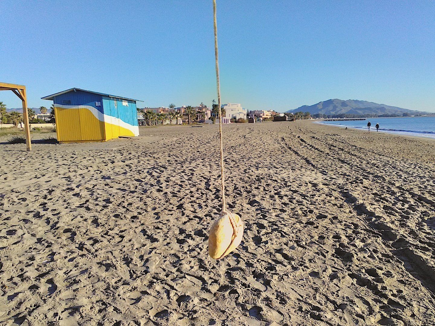 pebble dangling off a piece of string in the foreground with the wide sandy beach behind
