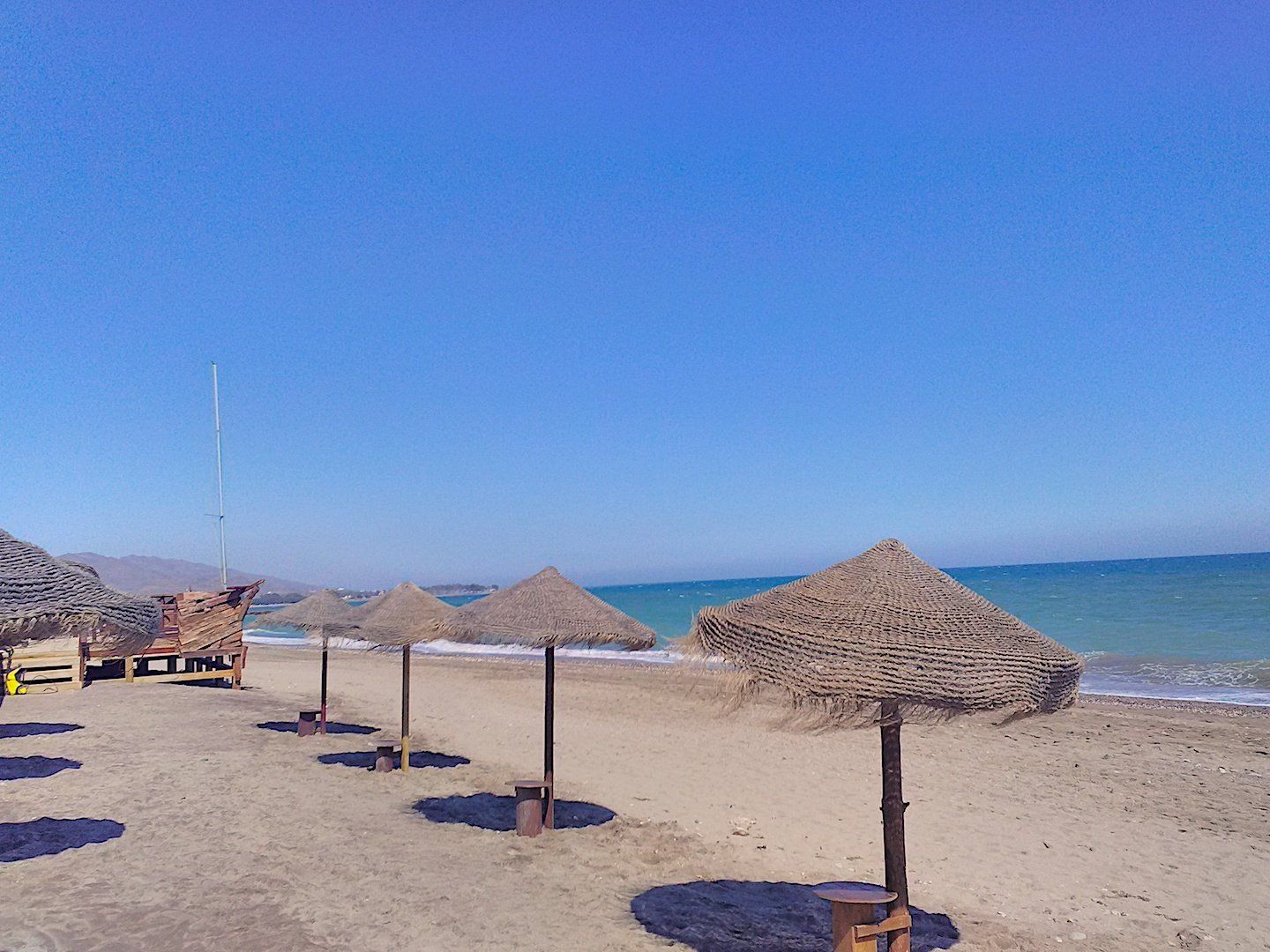 thatched sun parasols in a row on the sand and in the distant corner you can just see the edge of the wooden pirate bar