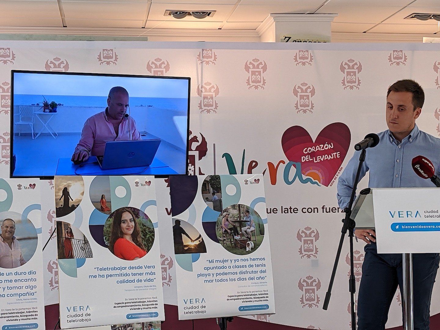 man stood at lectern with big screen behind him broadcasting a film