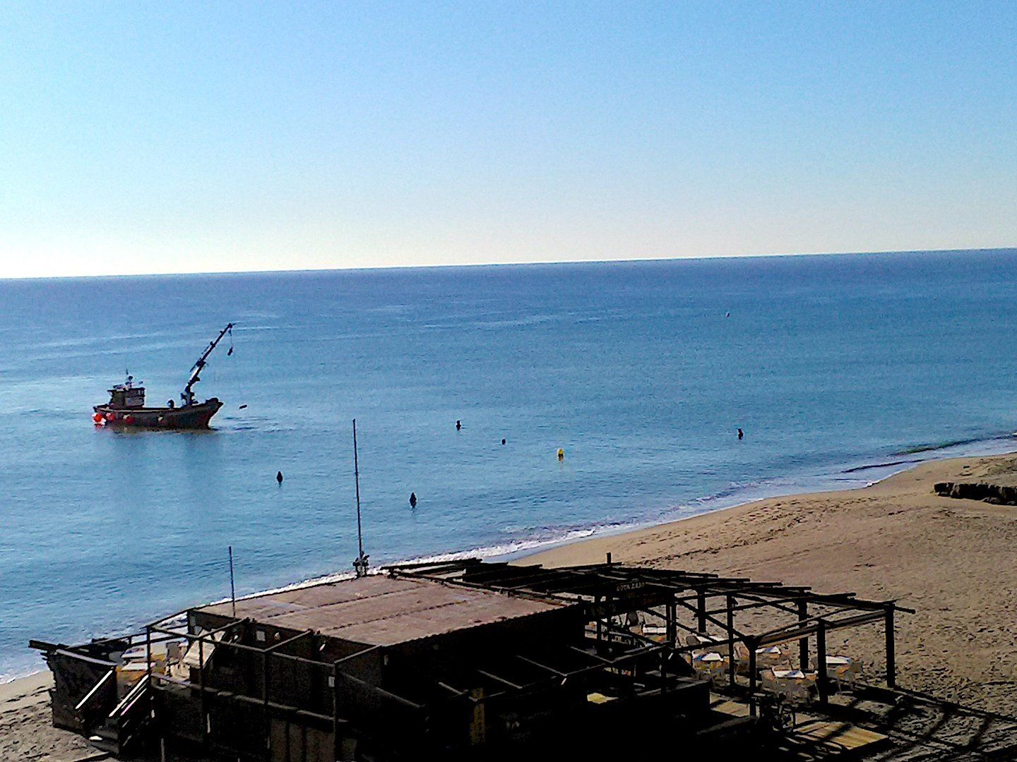 small boat with crane very close to shore is removing floats from the water