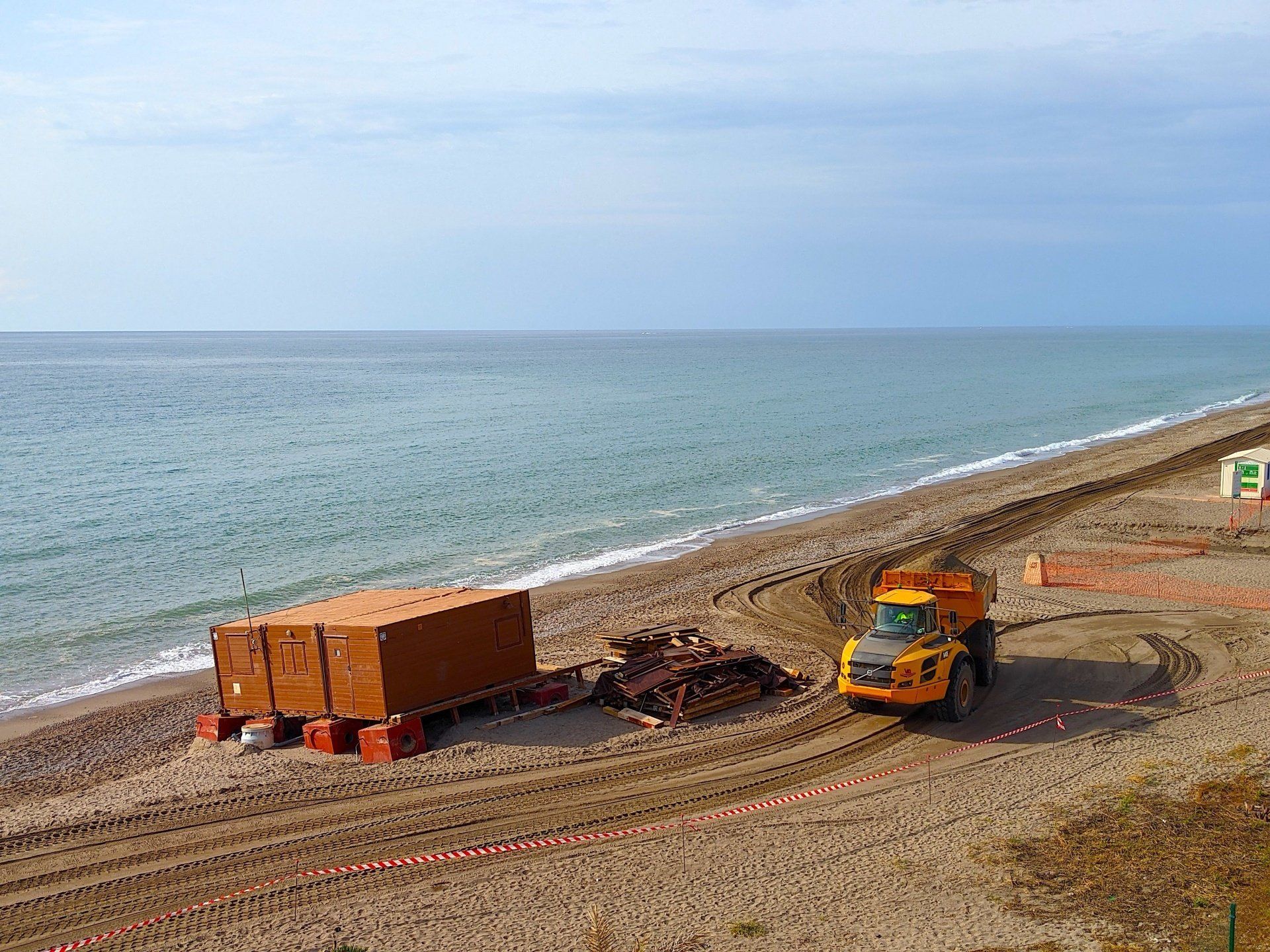a big dumper truck swerves around a beach shack on the beach below