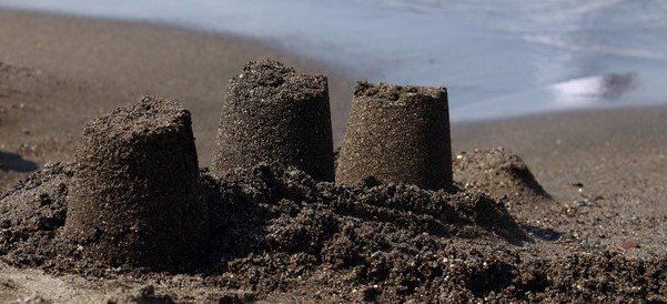 close up of three turrets of a sandcastle on the shoreline