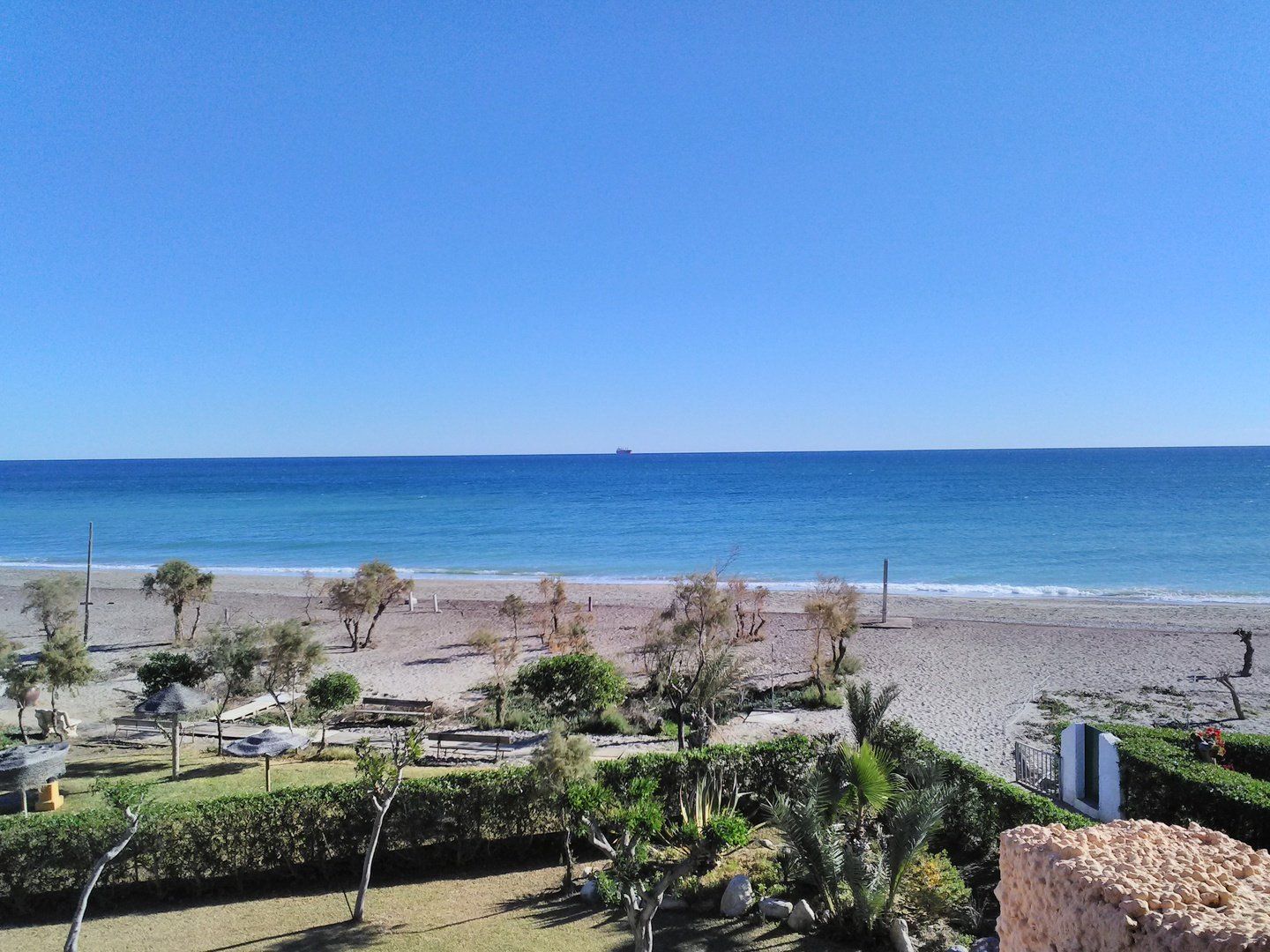 view from terrace looking down onto beach and sea with a ship on the horizon