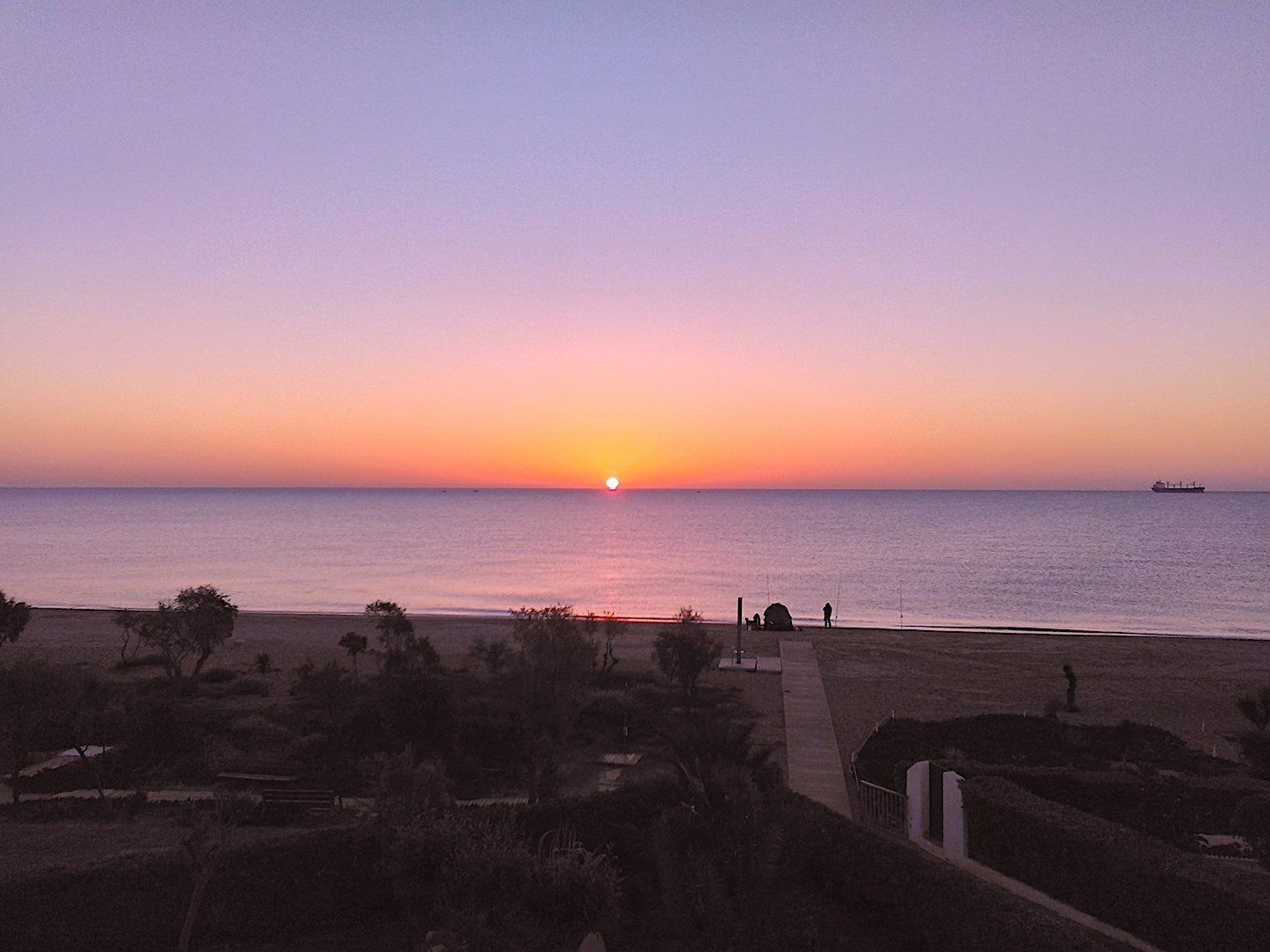 dawn and the sun is rising on the horizon making the sky purple while there is a fishermans tent on the beach at the end of the path
