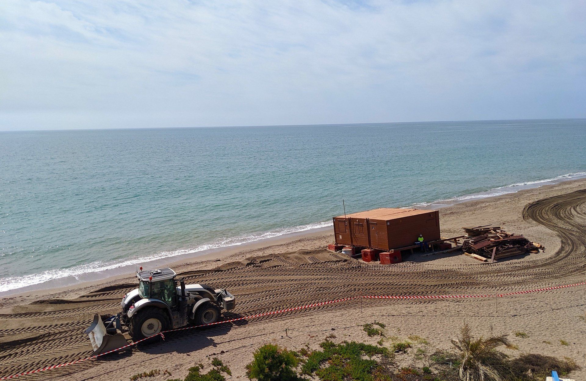 a big tractor on the beach heading towards a wooden beach bar by the waters edge