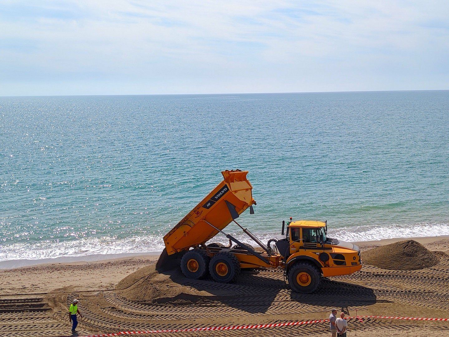 a big dumper truck empties its load on the sea shore