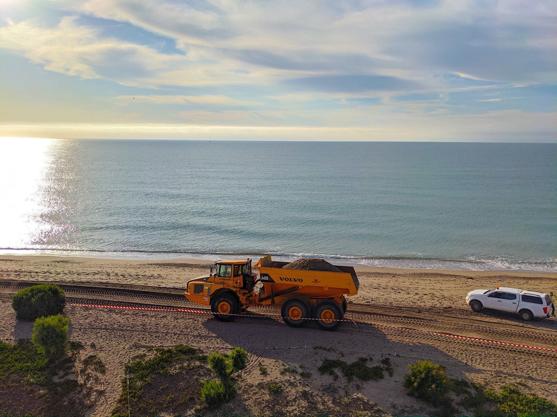 a big dumper truck drives along the seashore at low light