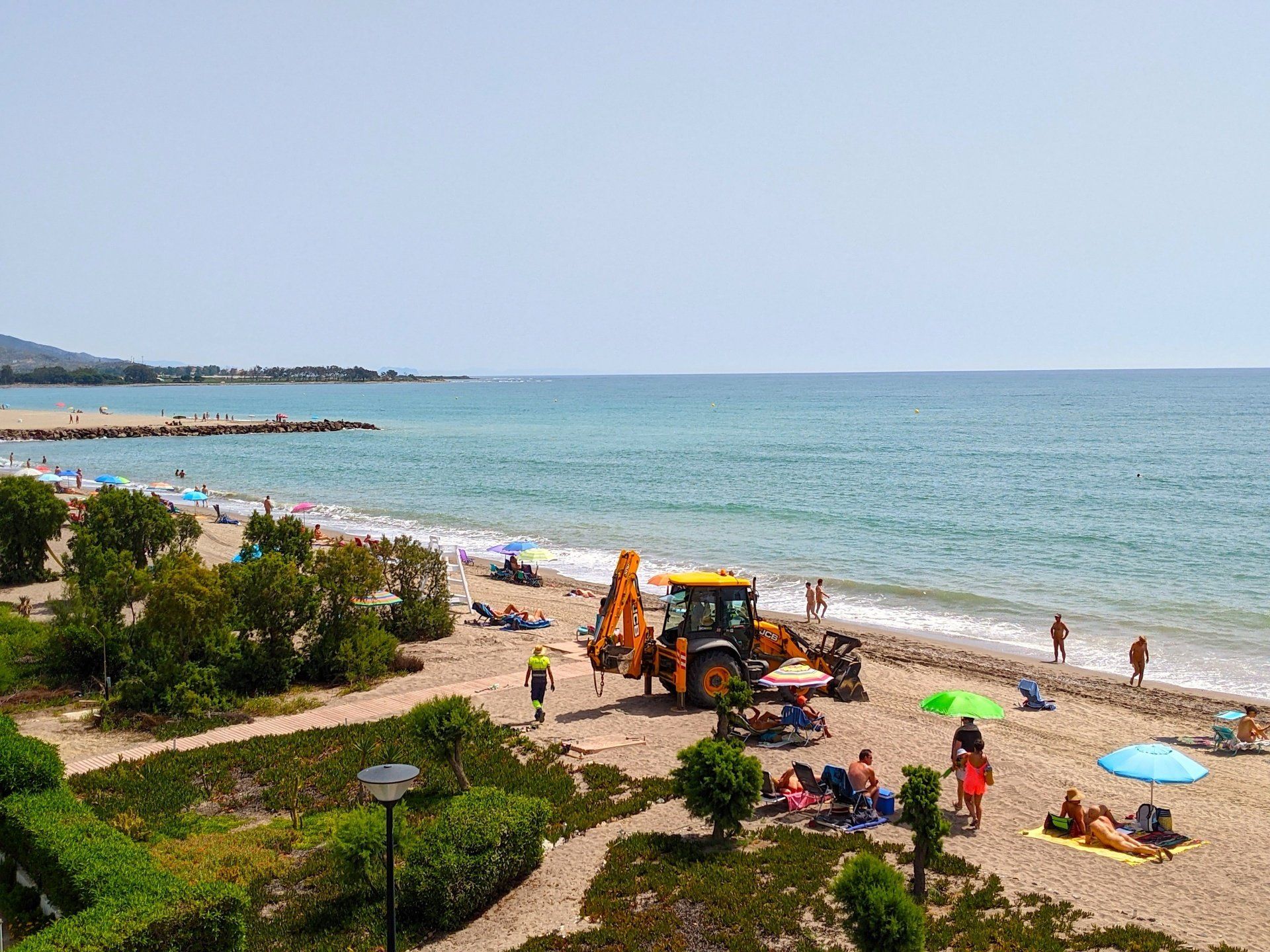 looking down onto the beach from above workmen and their machinery are at work while naked people sunbathe on the sand
