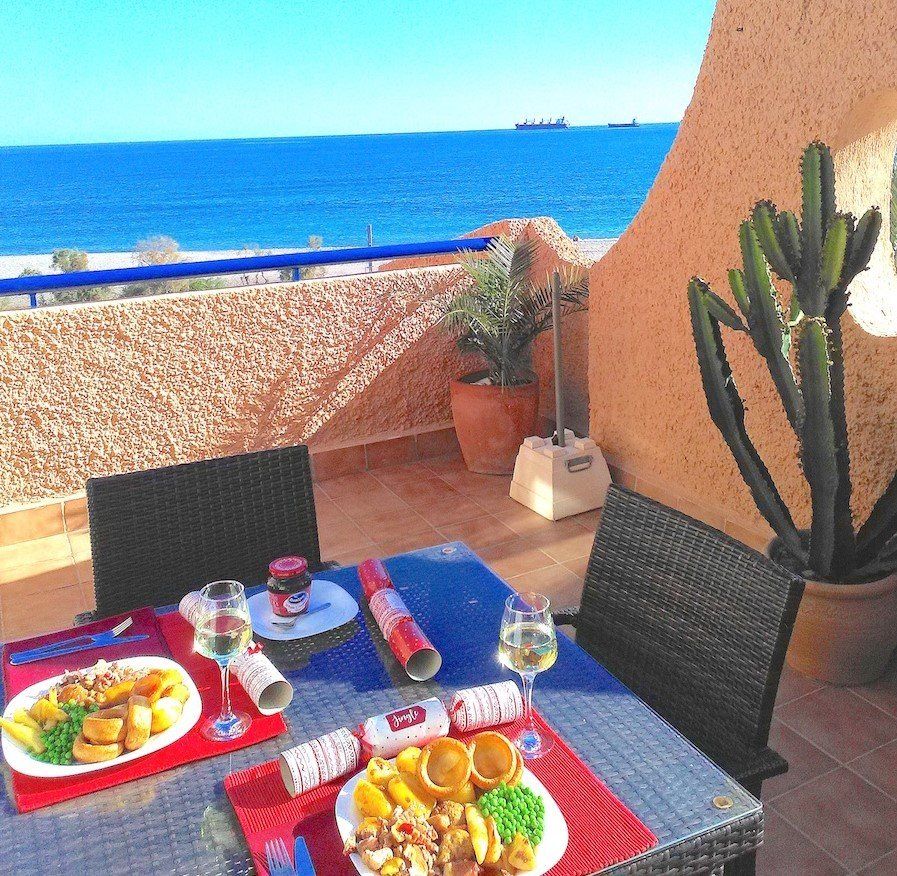 outside on the terrace with a sea view and there is a table with two plates of christmas lunch and two glasses of cava