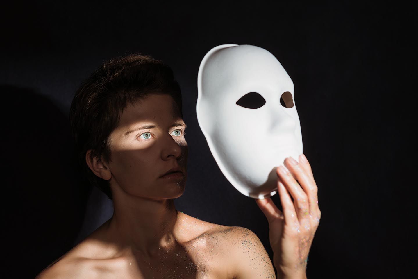 Frau steht fast im Dunkeln und nimmt ihre Maske ab, während Licht ihre Augen erleuchtet, Symbol für Selbsterkenntnis und die Befreiung von Illusionen