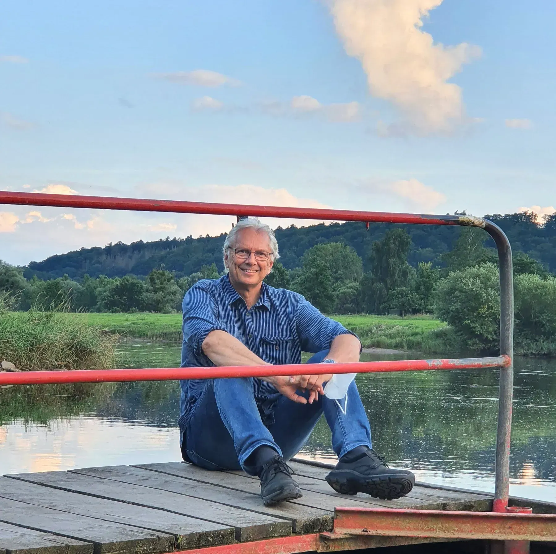 ückführungstherapeut entspannt sitzend an einem Fluss, Symbol für innere Ruhe und Verbindung zur Natur