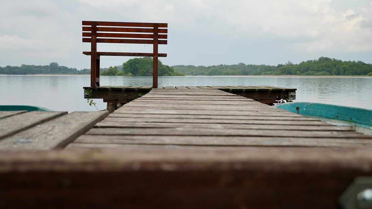 Eine einzelne Bank steht am Ende eines Steges mit Blick auf einen See - Praxis für Kunsttherapie Susanne Grön in Zarrentin.