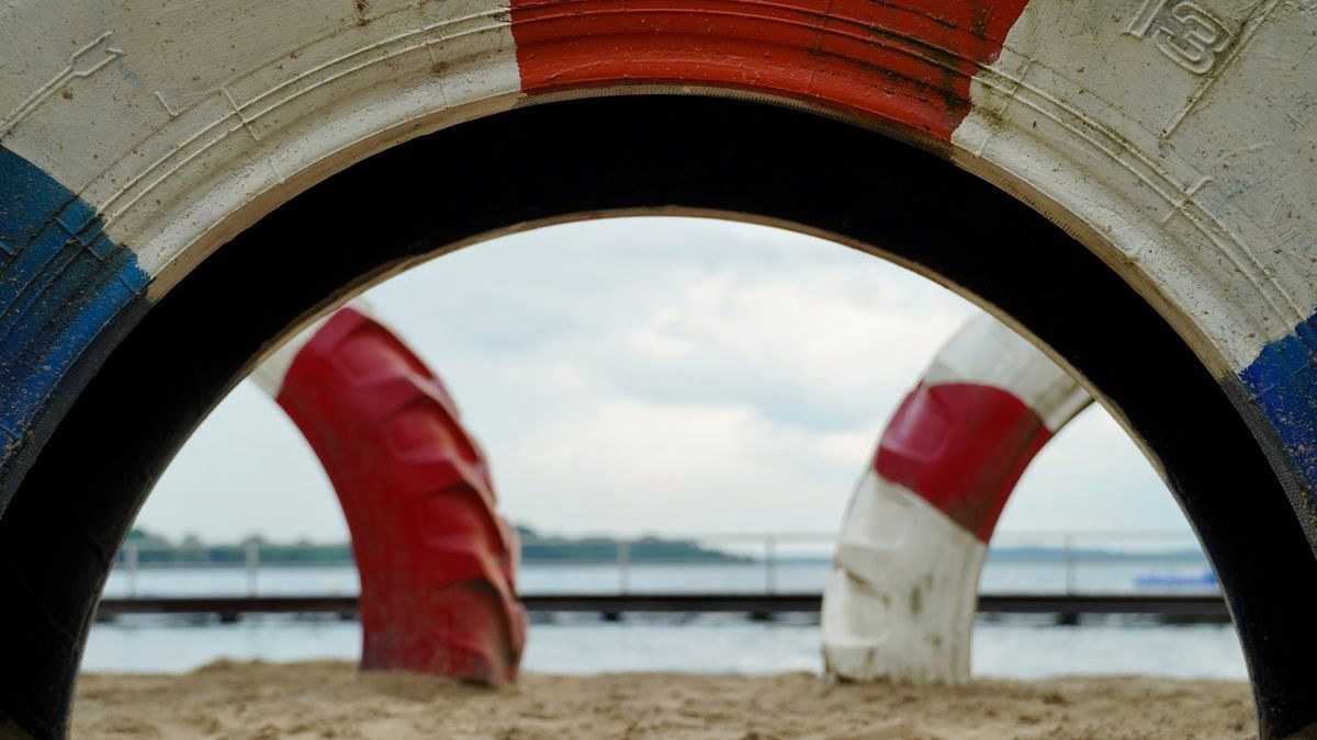 Blick durch einen bunt bemalten Autoreifen durch zu einem See mit Steg - Praxis für Kunsttherapie Susanne Grön in Zarrentin.