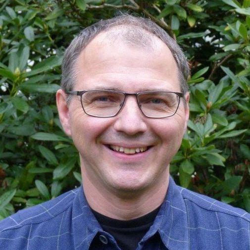 Bild von Stefan Krämer mit blauem Hemd vor grüner Hecke