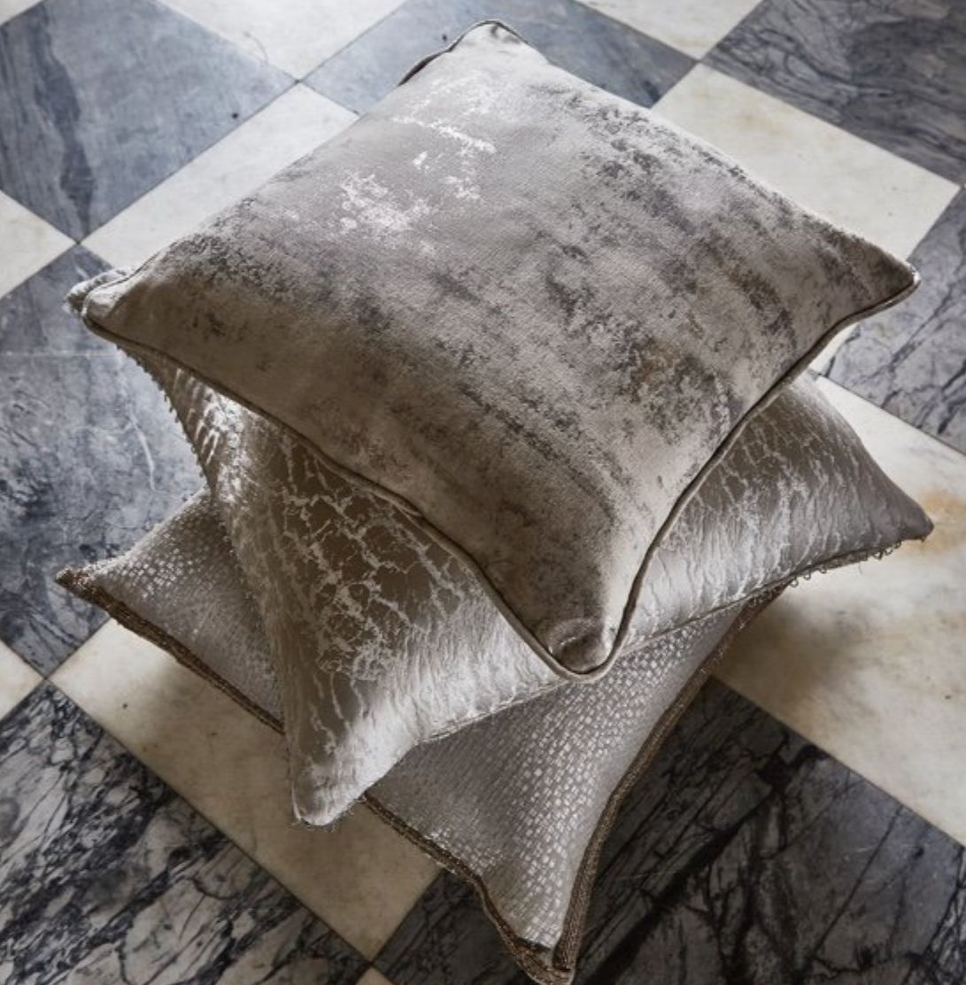 Paire de coussins Phoenix aux reflets métallisés argentés et dorés, aspect texturé luxueux sur sol en marbre.