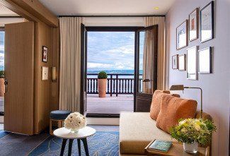 Salon de chambre d'hôtel avec canapé orange, balcon en bois et vue mer imprenable.