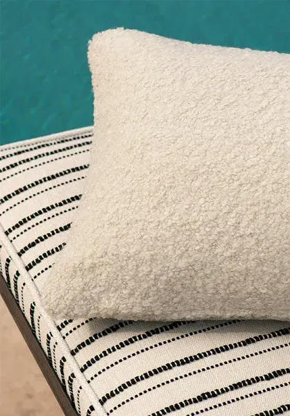 Gros plan sur un coussin bouclé blanc à côté d'un coussin rayé, collection Misia Evasion.