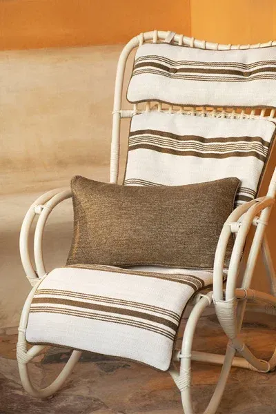 Fauteuil lounge en rotin blanc avec coussins rayés Misia Evasion dans une ambiance estivale ocre.