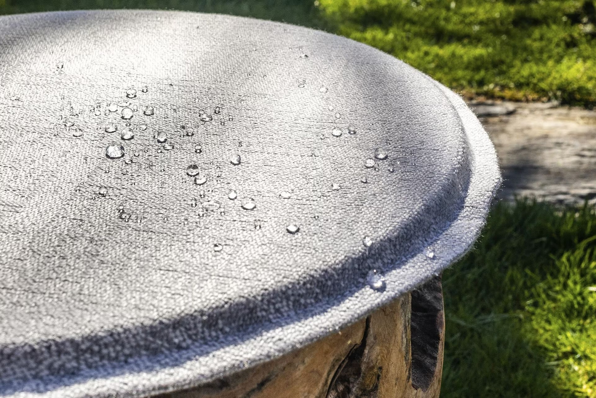 Gros plan d'une surface textile grise Agora Signature avec gouttes d'eau perlantes en extérieur.