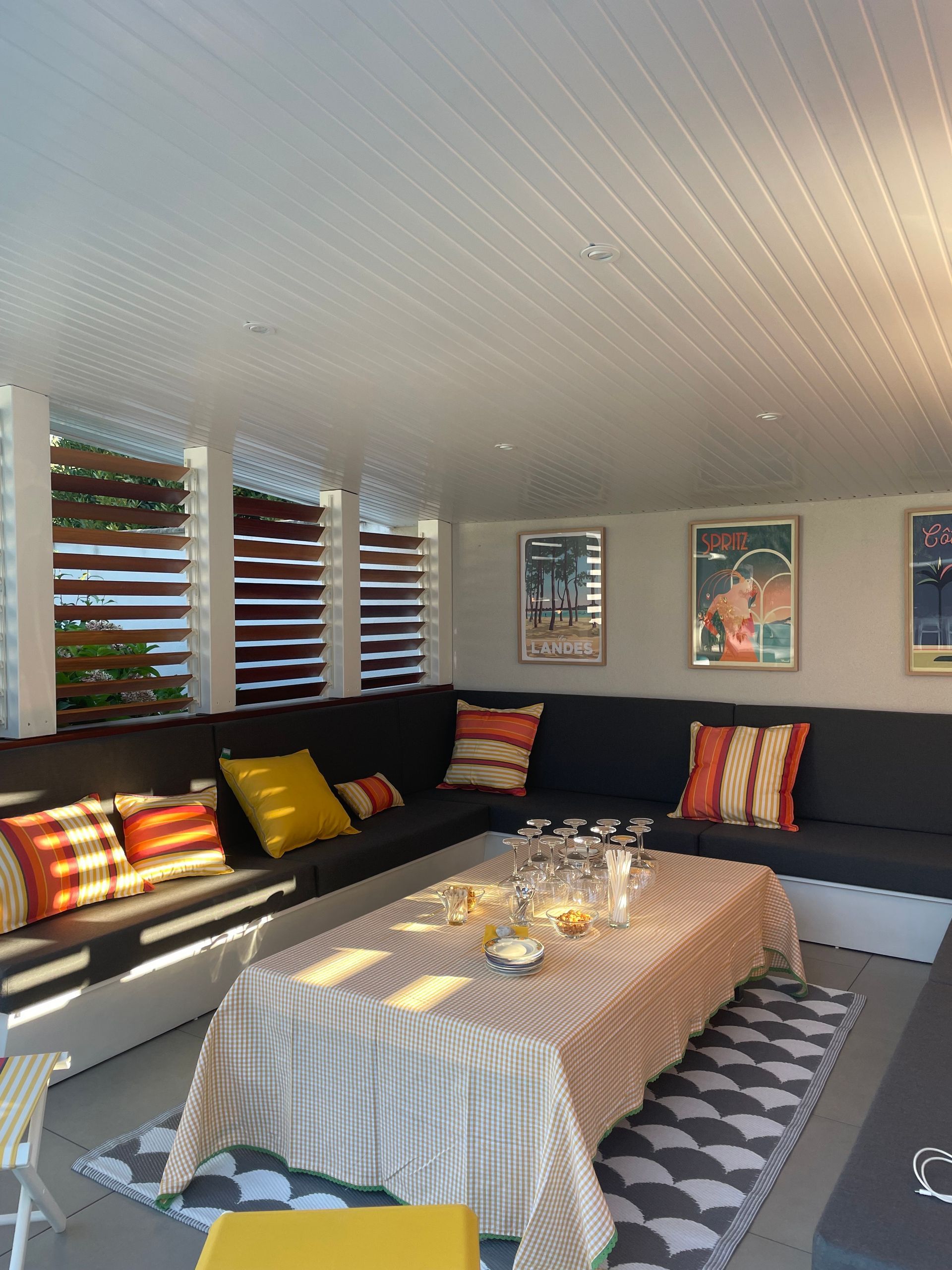 Coussins de banquette jaune et orange rayés sur mesure pour un aménagement d'angle sous une véranda lumineuse.