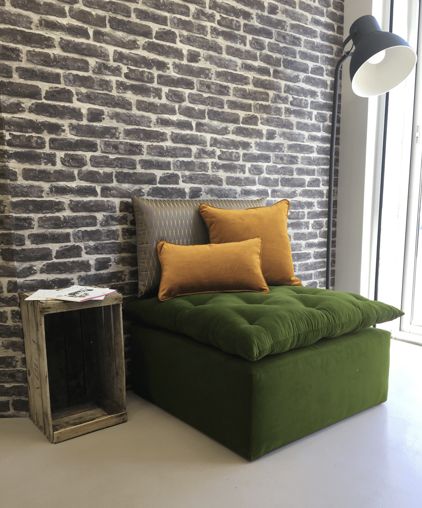 Ambiance cosy avec un lit, des coussins ocre et jaune moutarde sur fond de mur en briques grises.