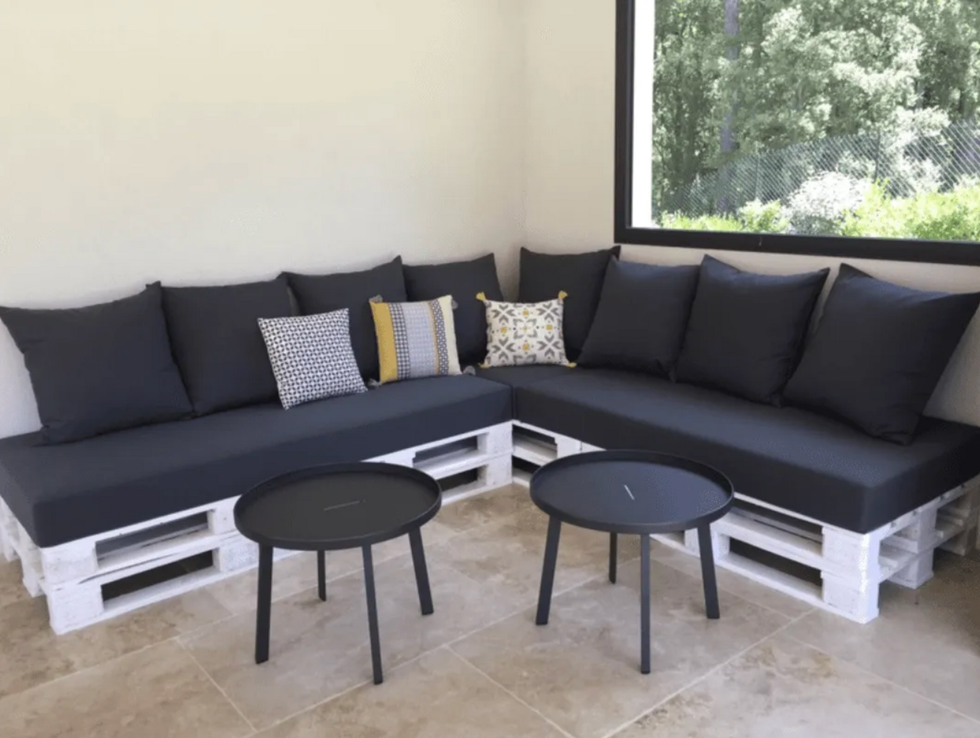 Coussins d'assise et de dossier noirs sur mesure pour l'aménagement d'un canapé d'angle extérieur en palettes blanches.