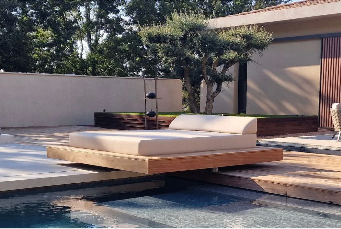 Épais matelas extérieur beige sur mesure pour un lit de repos en lévitation au bord de l'eau.