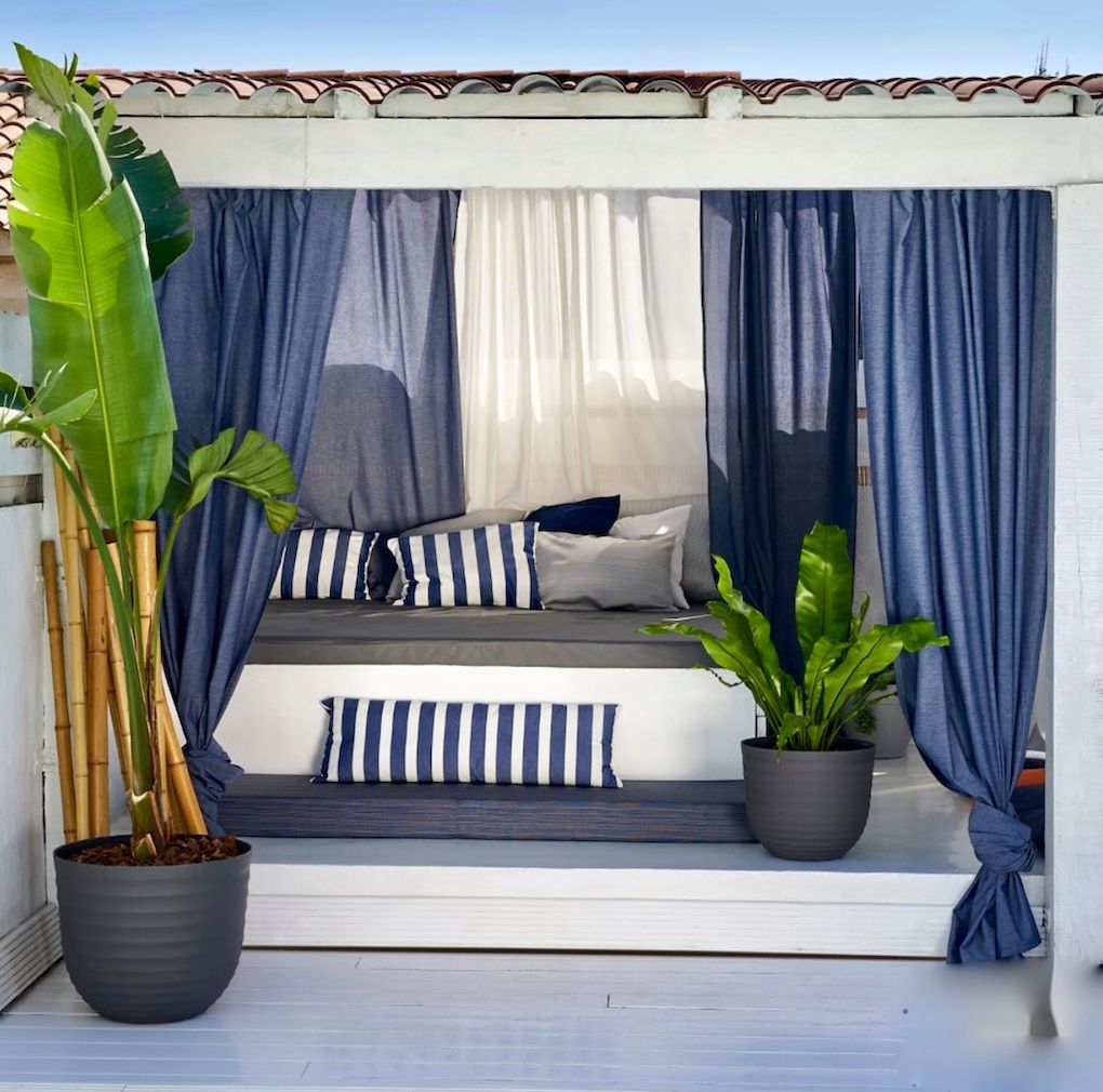 Espace lounge extérieur avec rideaux bleus et blancs et coussins assortis pour une terrasse d'été.