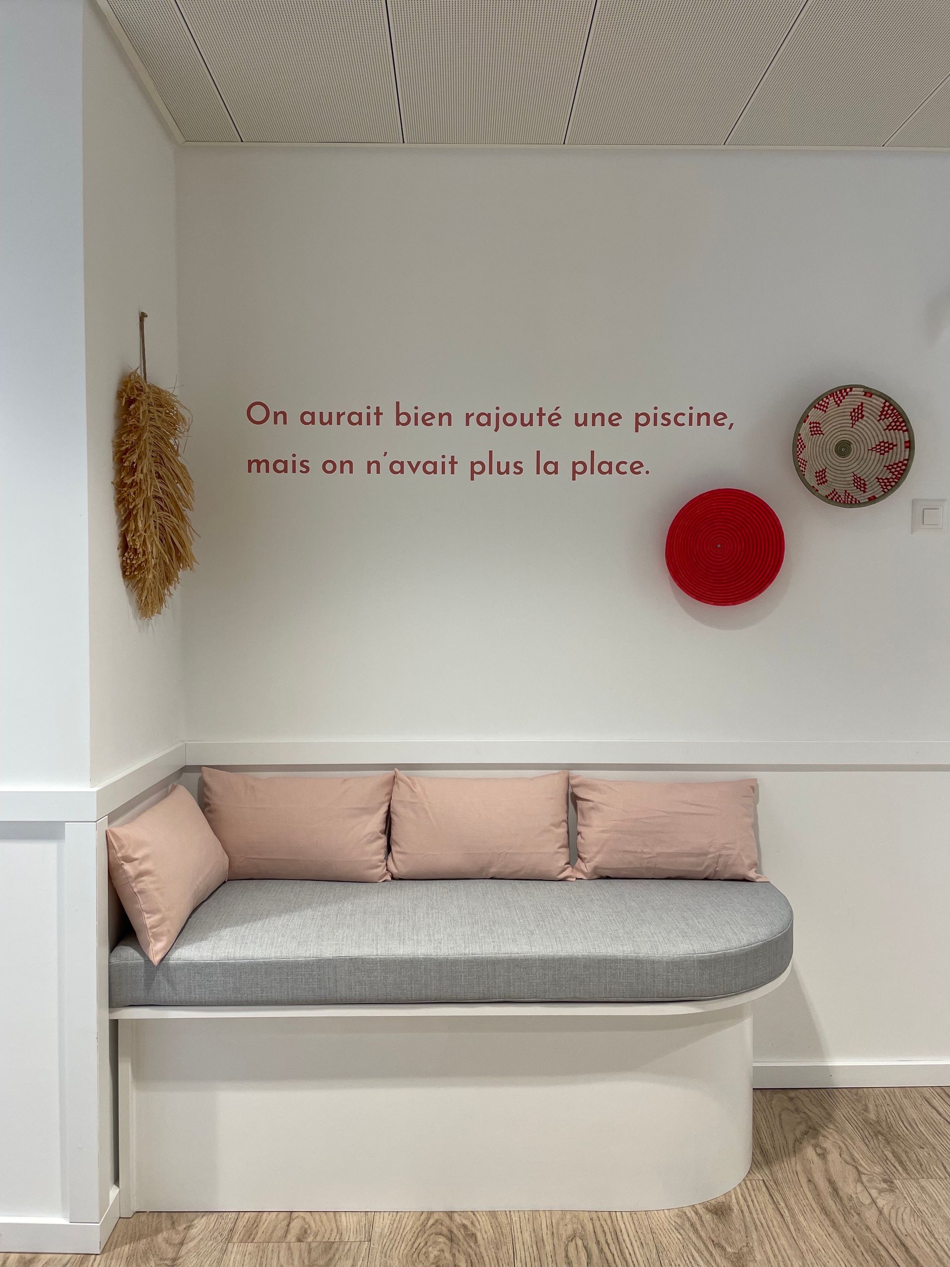 Banquette sur mesure arrondie en tissu gris clair avec coussins rose poudré, coin lecture chez un particulier – réalisation Mousse et Confection