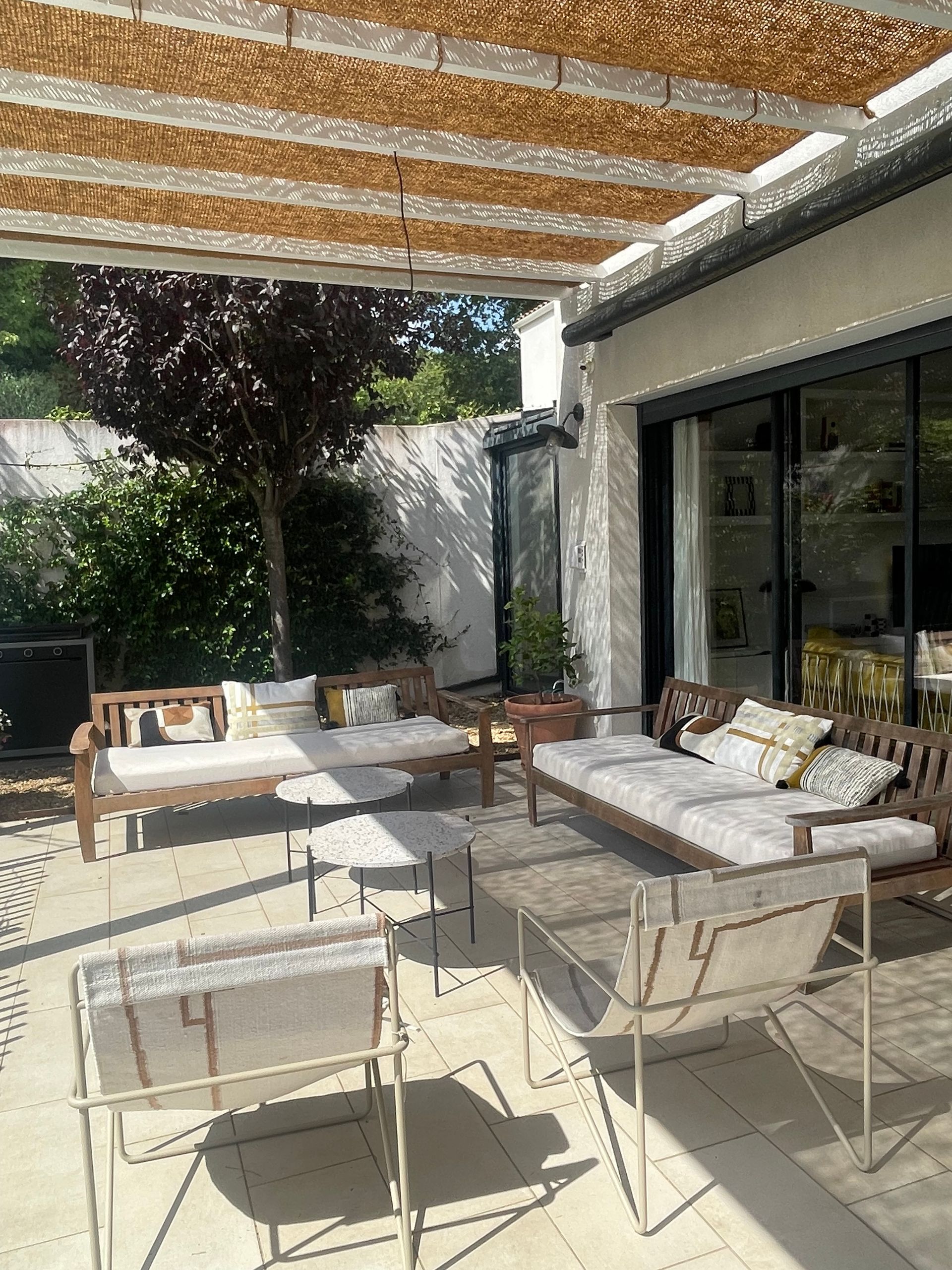 Coussins et matelas beiges sur mesure pour des chaises et canapés sous une pergola en cannisse typique.