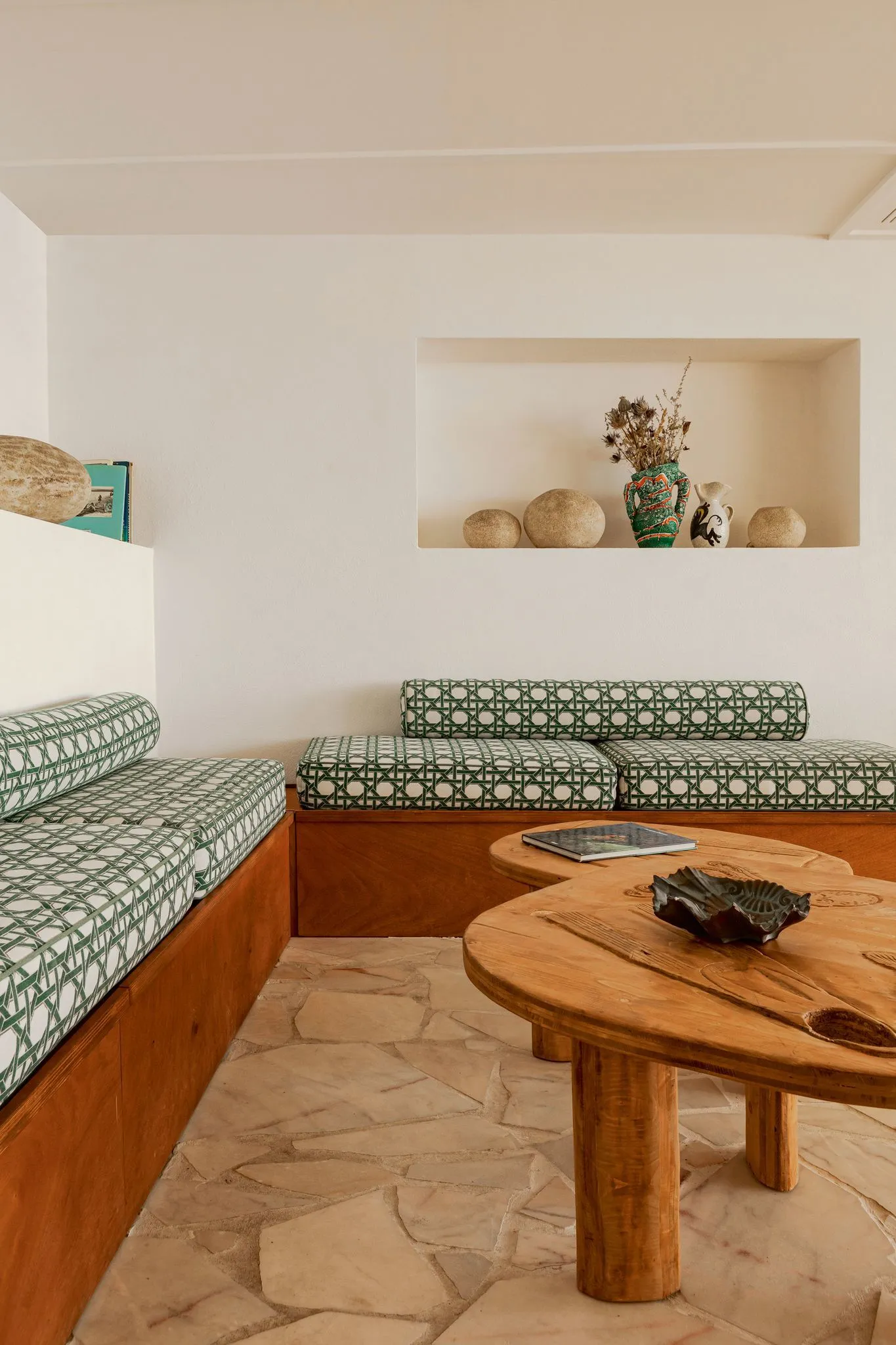 Coussins sur mesure en tissu motif cannage vert et blanc sur banquette bois d'angle, salon méditerranéen au sol en pierre – réalisation Mousse et Confection