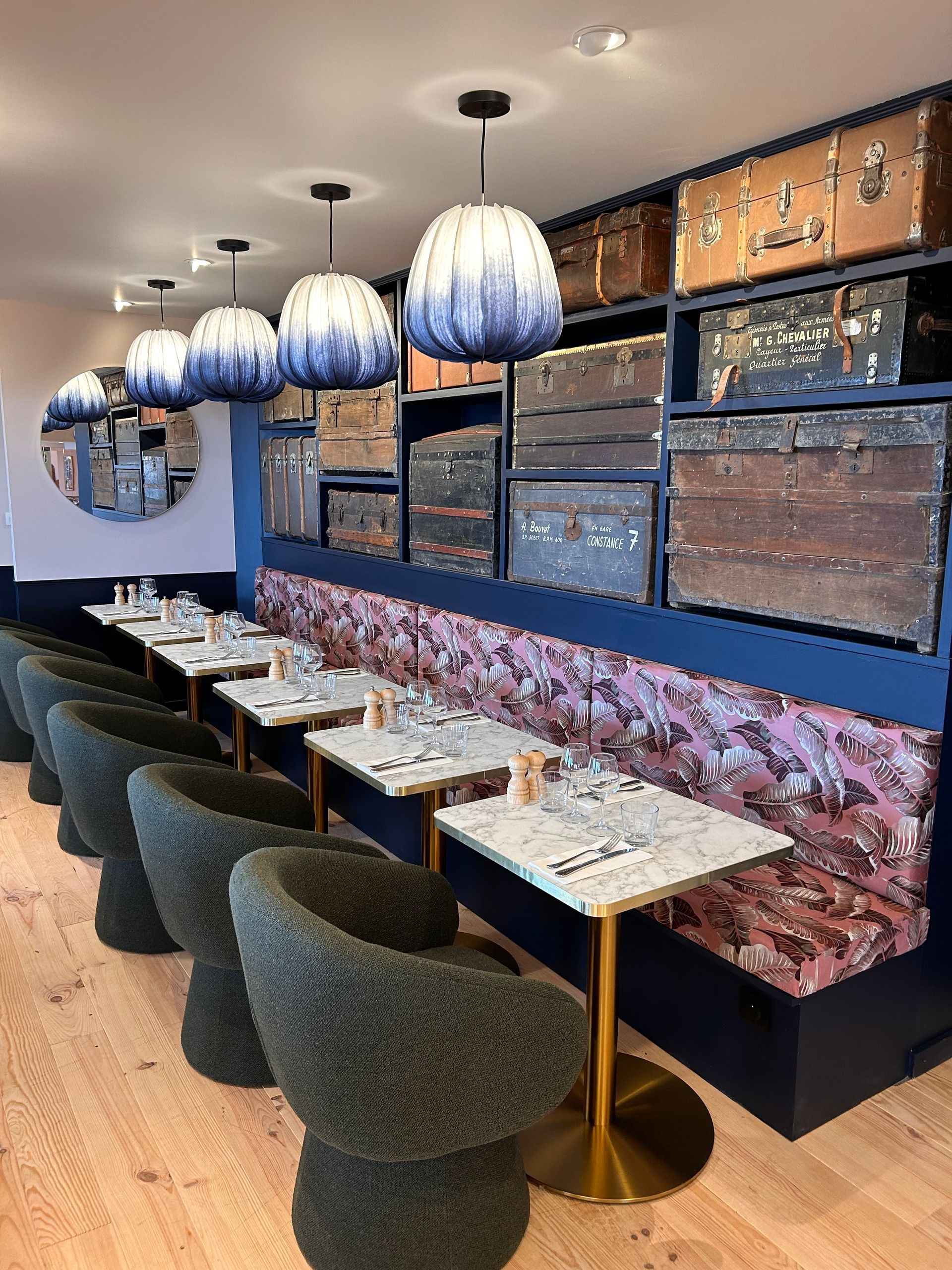 Alignement de suspensions en tissu bleu dégradé devant un mur décoratif composé de malles de voyage anciennes.