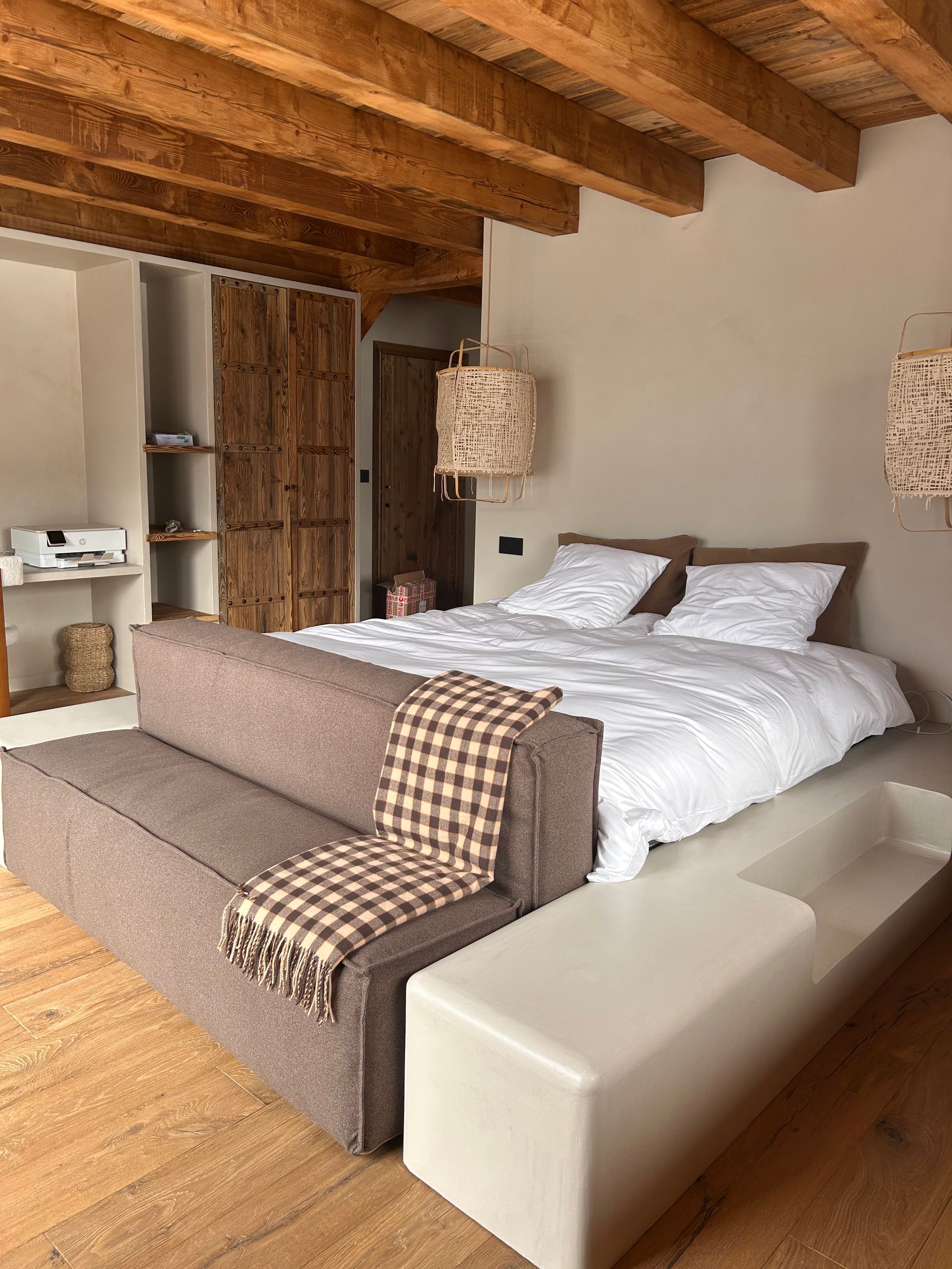 Décoration de chambre naturelle avec poutres en bois apparentes, rangements intégrés et luminaires en osier.