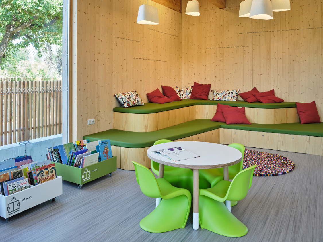 Banquette d'angle sur mesure verte avec nombreux coussins rouges pour un espace lecture et détente enfant.