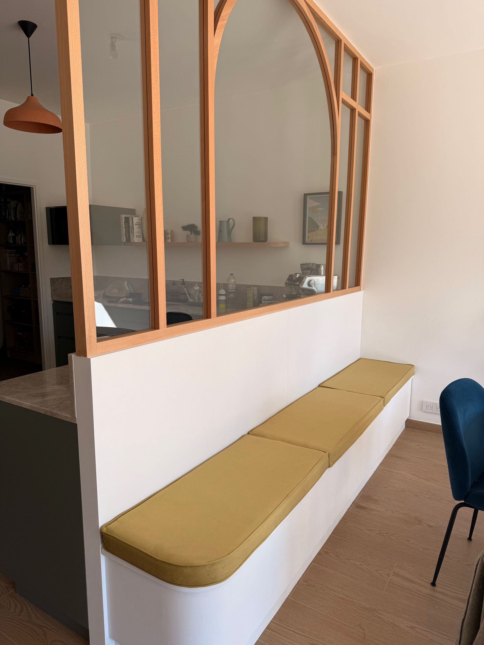 Long coussin d'assise sur mesure jaune moutarde pour une banquette installée sous une verrière intérieure.