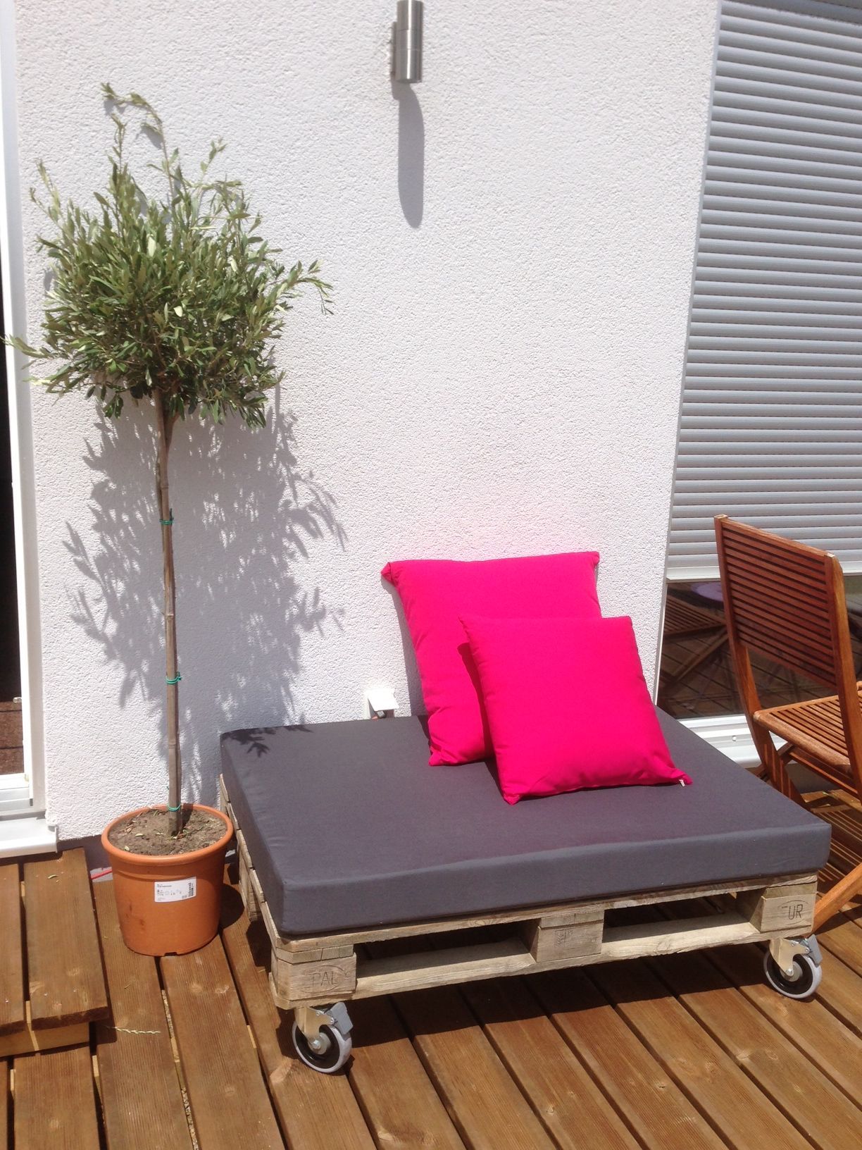 Coussin d'assise gris anthracite et coussins roses sur mesure pour un petit pouf extérieur en palette.