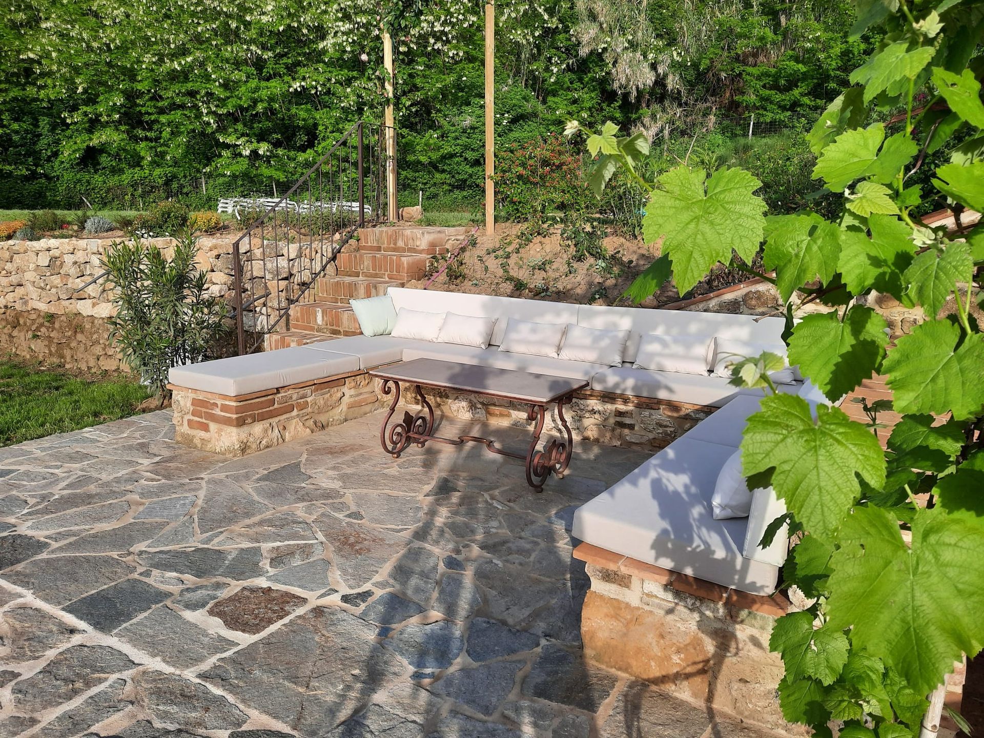 Coussins d'assise sur mesure pour une banquette maçonnée courbée sous une tonnelle ombragée par des vignes.