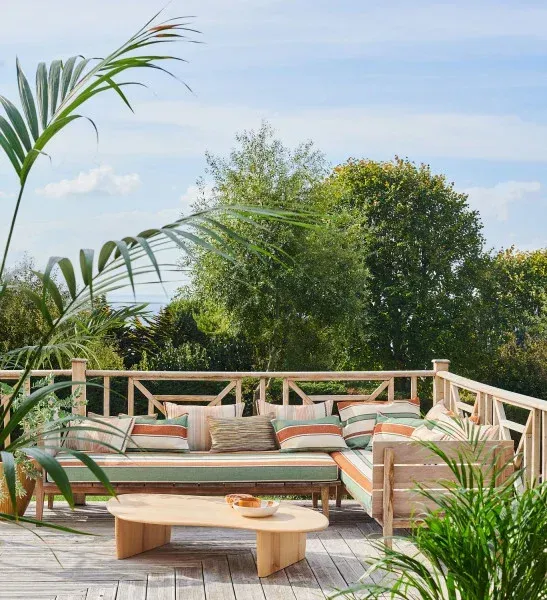 Ambiance extérieure avec feuillage tropical et ciel bleu, présentant la collection de tissus d'été Casamance.